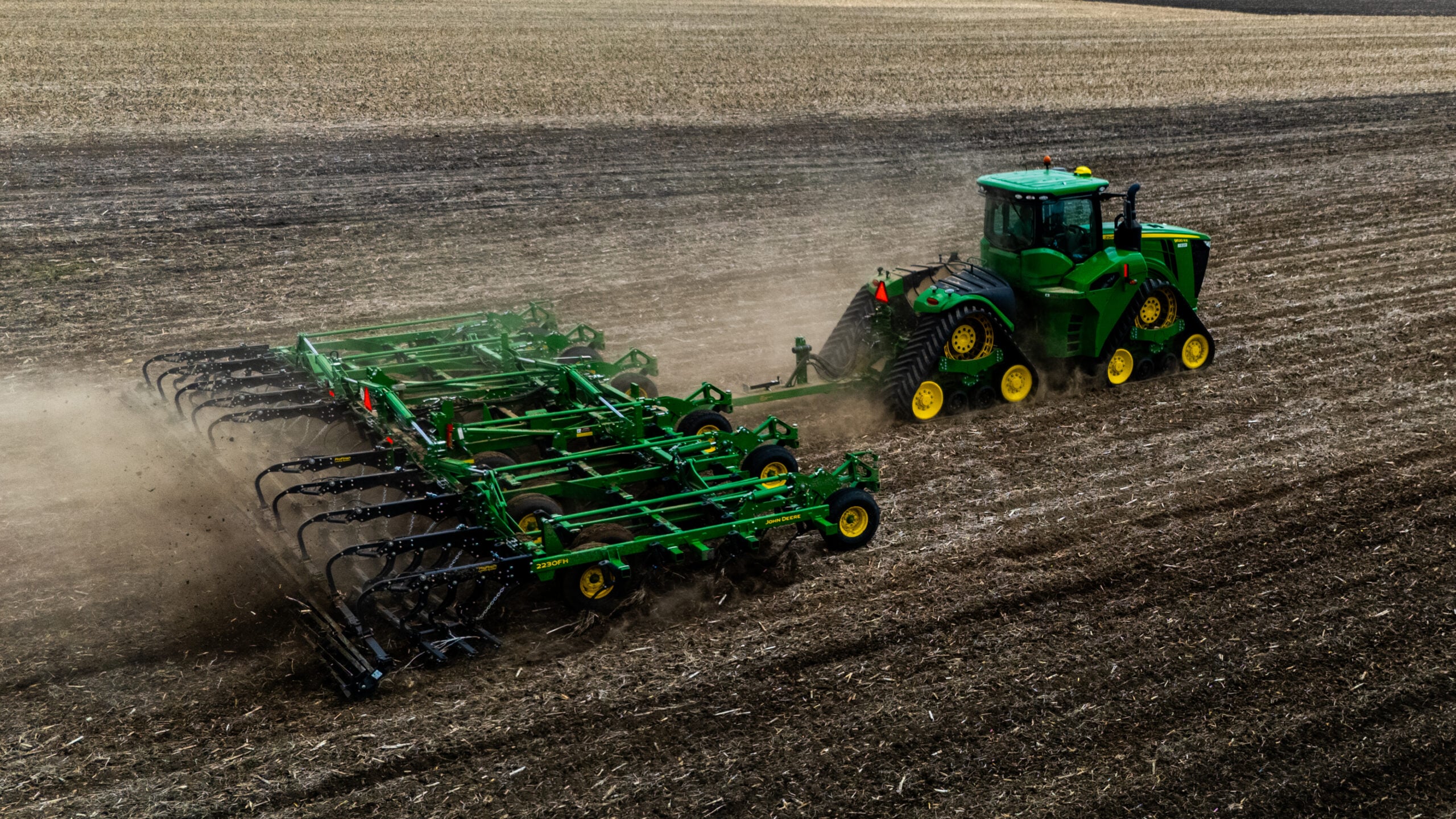 Close-up drone photo of green tractor pulling large field cultivator with dust trail during spring tillage in Morgan County Illinois