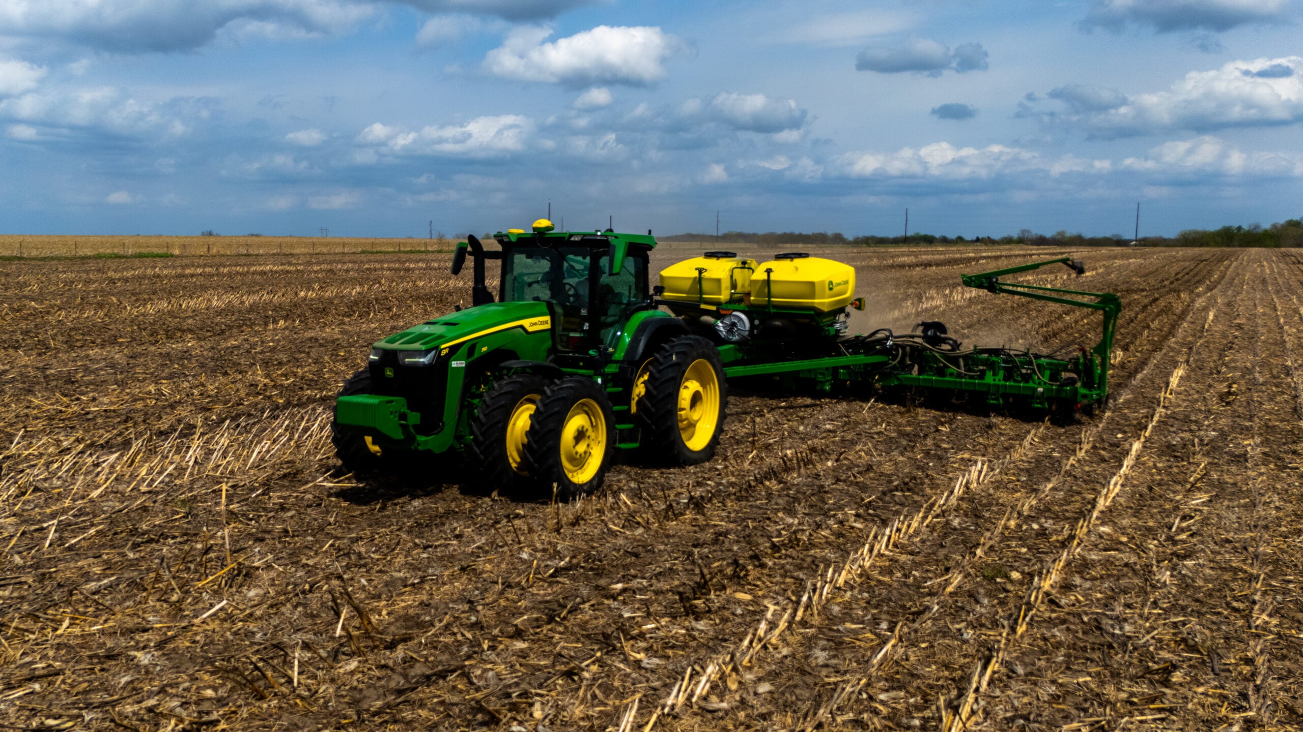 Low altitude drone photo of John Deere tractor and planter close up with dramatic cumulus clouds over Central Illinois farmland during spring planting