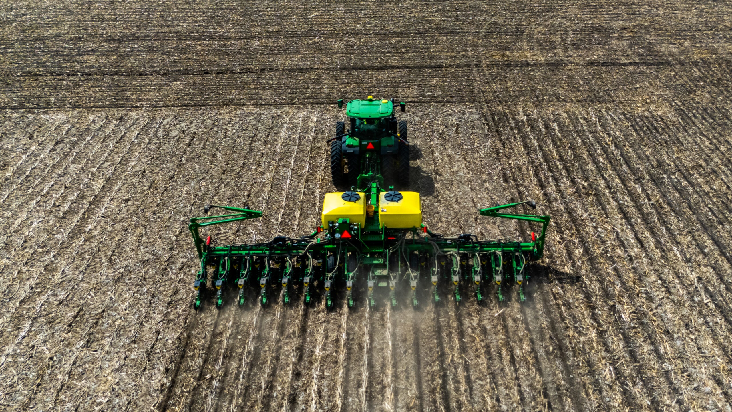 Overhead drone photo of tractor and multi-row planter from directly above showing full width of planting units working Illinois field during spring planting season