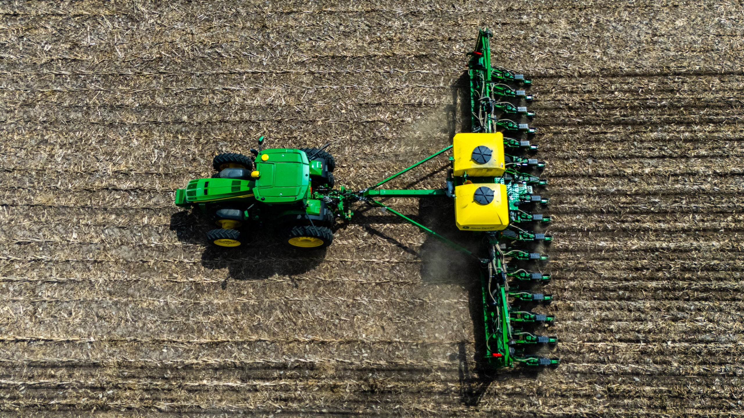 Top-down drone photo of John Deere planter with yellow seed boxes casting shadow on corn stubble field in Morgan County Illinois