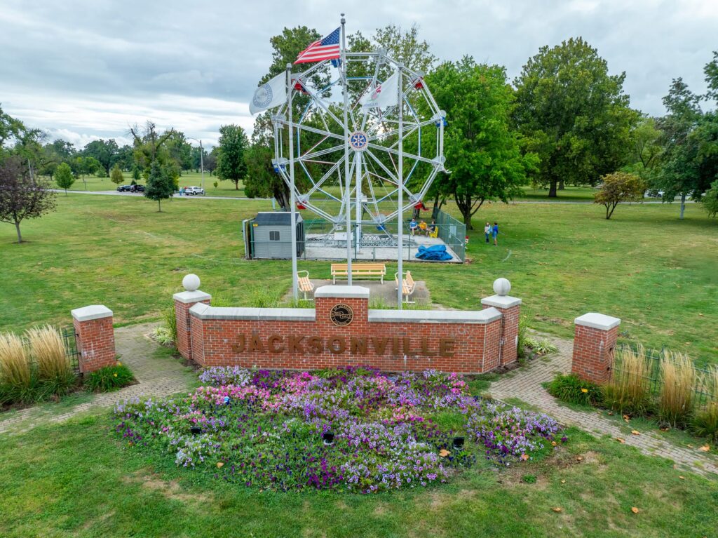 Aerial drone photo of the Big Eli Ferris Wheel behind the brick Jacksonville Illinois welcome sign and flower beds in Community Park