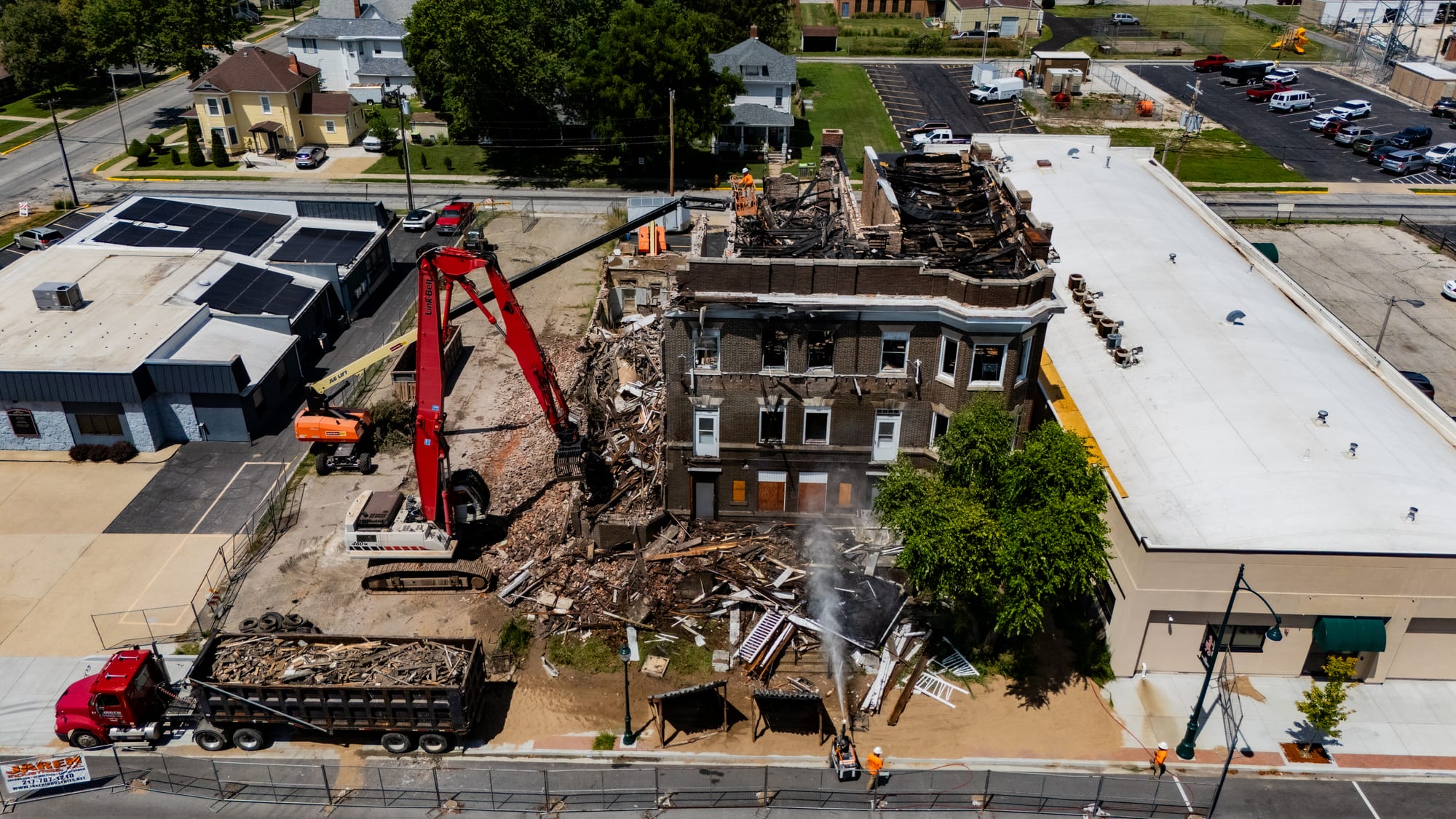 Drone view of the fire-gutted Cherry Apartments on West State Street Jacksonville IL with demolition excavator, dump truck, and dust suppression spray