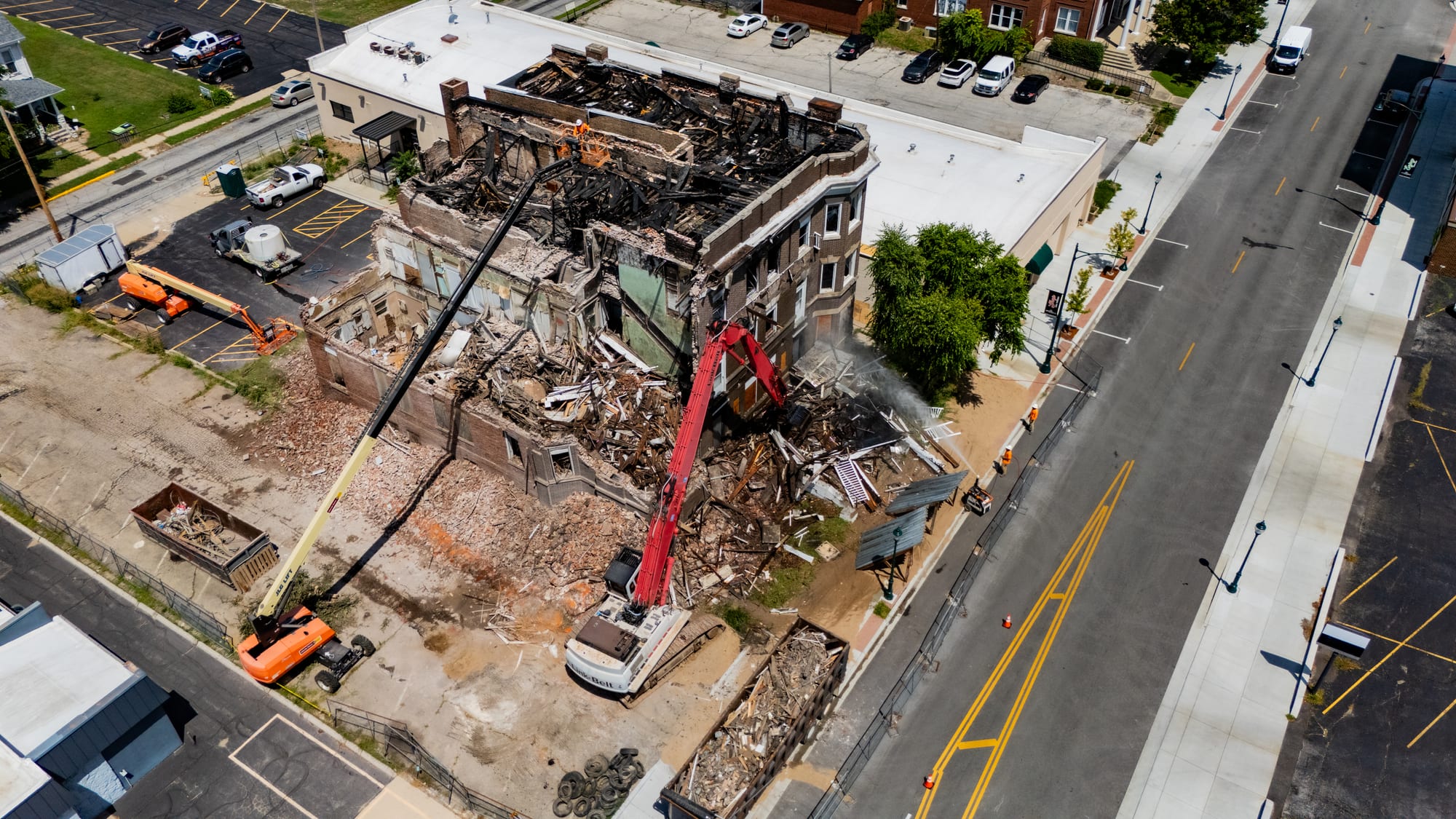 Wide drone photo of the Cherry Apartments demolition on West State Street Jacksonville IL with debris trucks and JLG lifts staged around the site