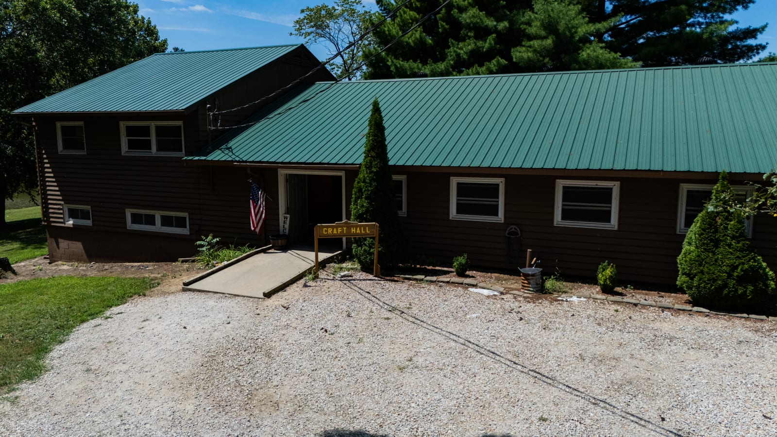 Craft Hall lodge with American flag at Western Illinois Youth Camp, aerial drone view of the log building and green metal roof