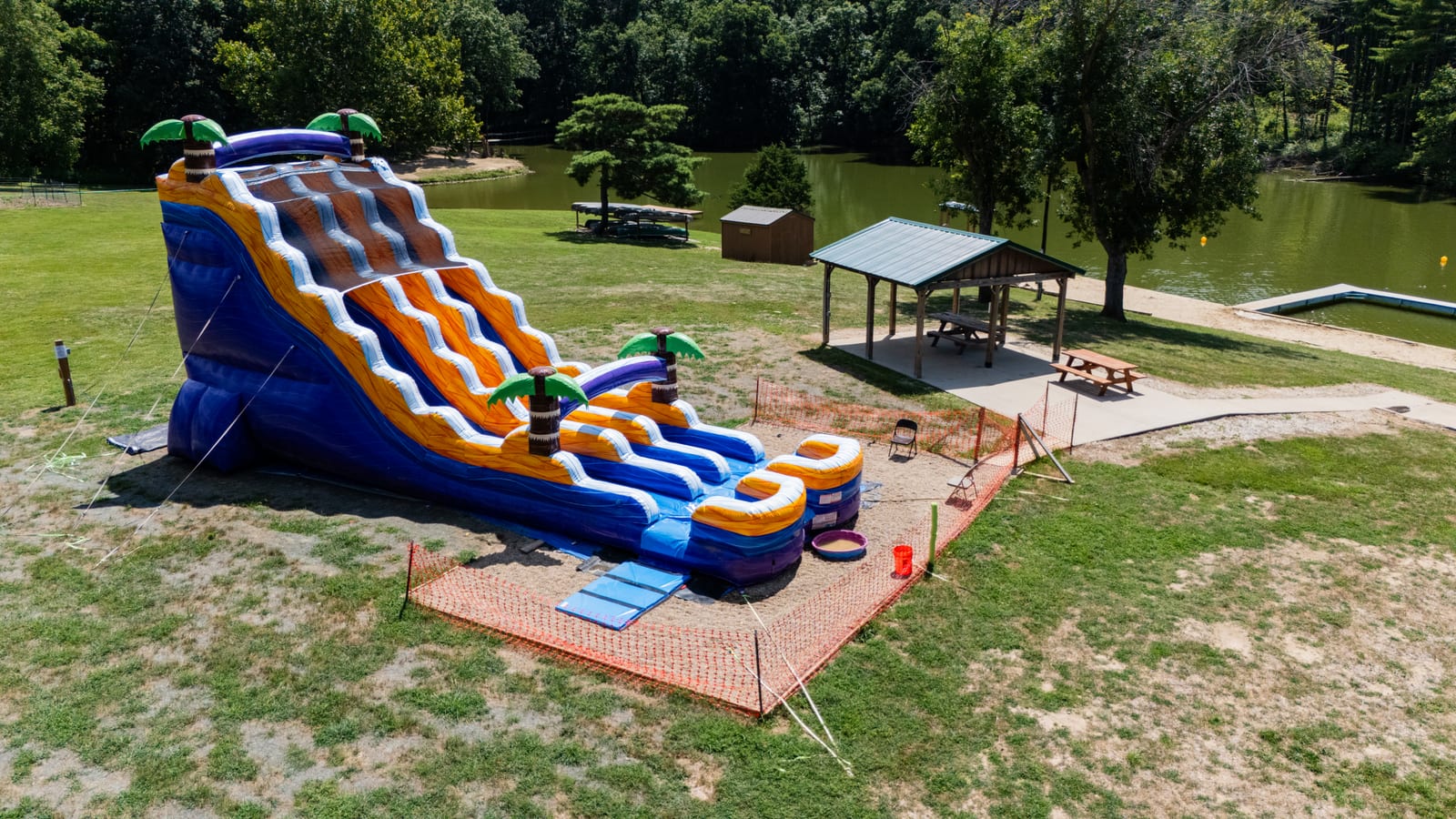 The brand-new inflatable waterslide at Western Illinois Youth Camp with palm-tree towers and picnic shelter beside Lake Jacksonville