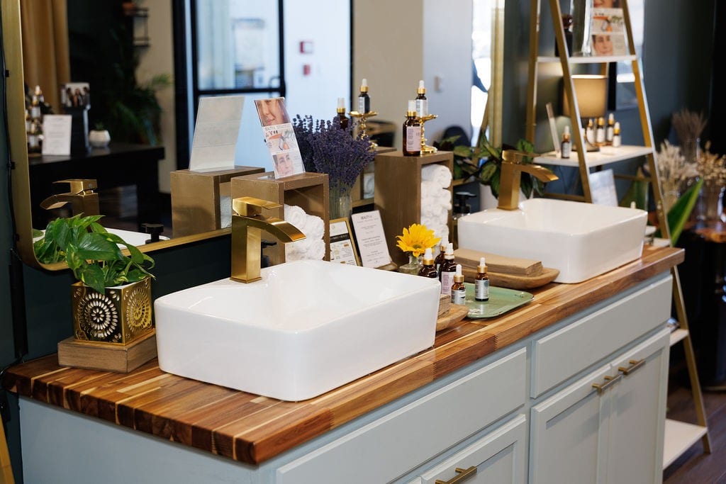 Brass-fixture vessel sinks and botanical skincare testing bar inside Cheryl Kelly & Co. in Jacksonville Illinois
