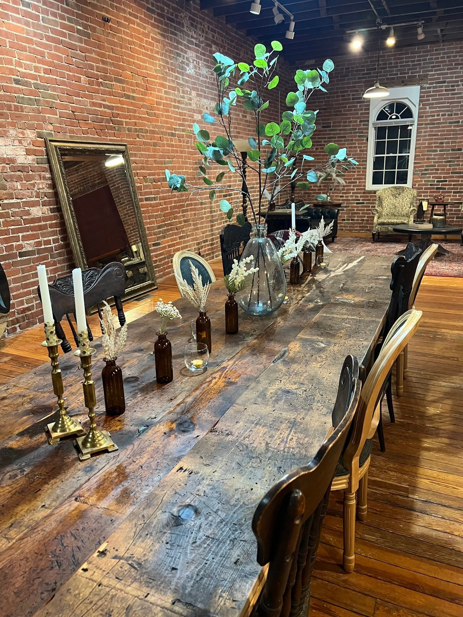 Custom reclaimed wood farmhouse table set with glassware and greenery beside a brick wall at The Transfer Co. Event Space in Jacksonville, Illinois