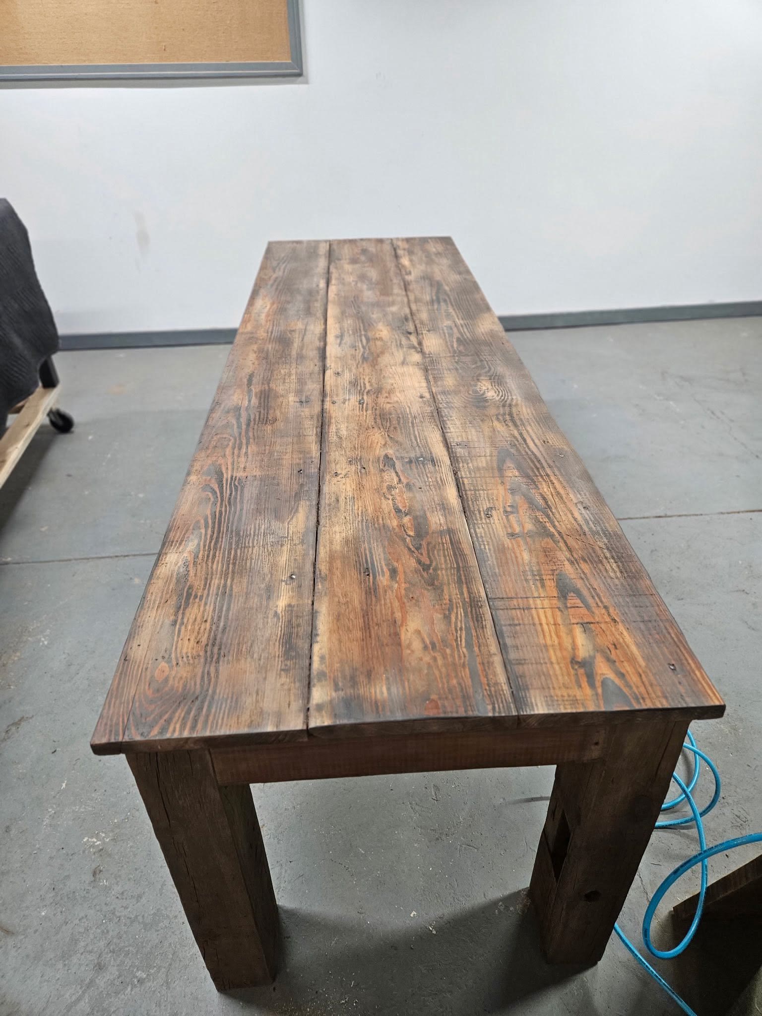 Long reclaimed wood farmhouse table standing in the Jacksonville Transfer Company woodworking shop with lumber racks behind it, Jacksonville, Illinois