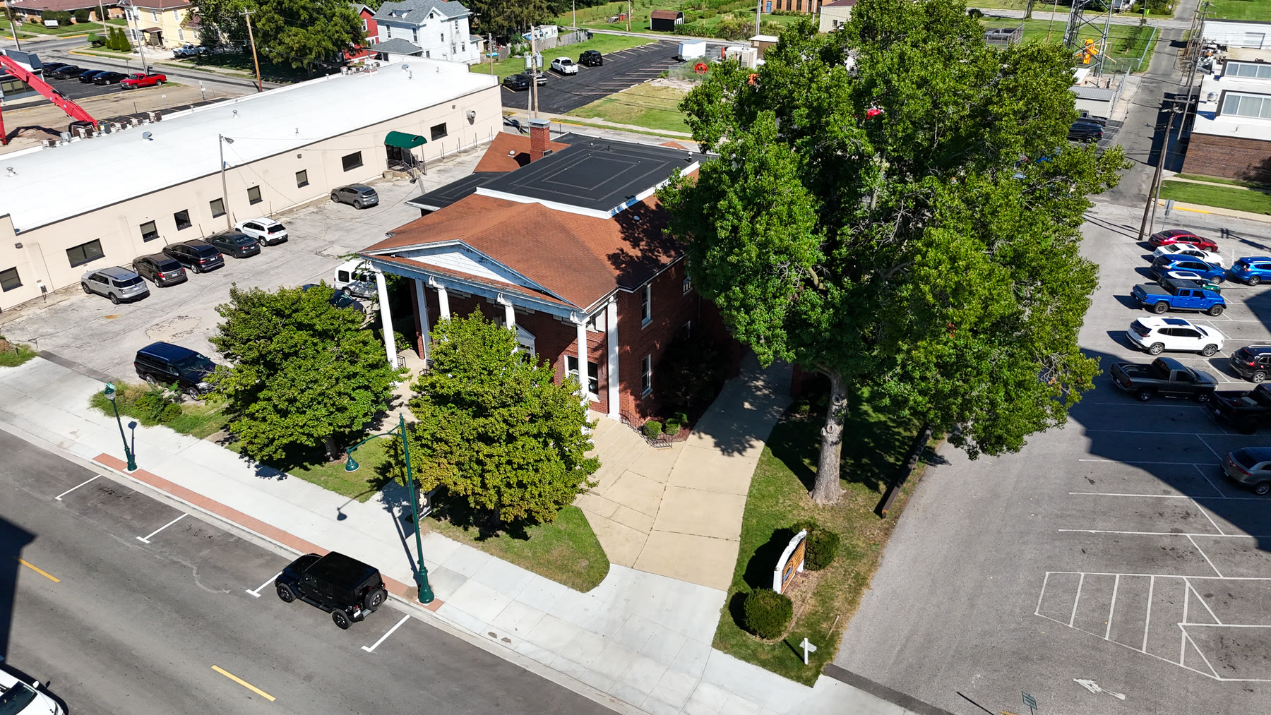 Aerial drone photo looking down on the front of the Gillham House, its columned porch, shade trees, and the West State Street sidewalk in downtown Jacksonville, Illinois