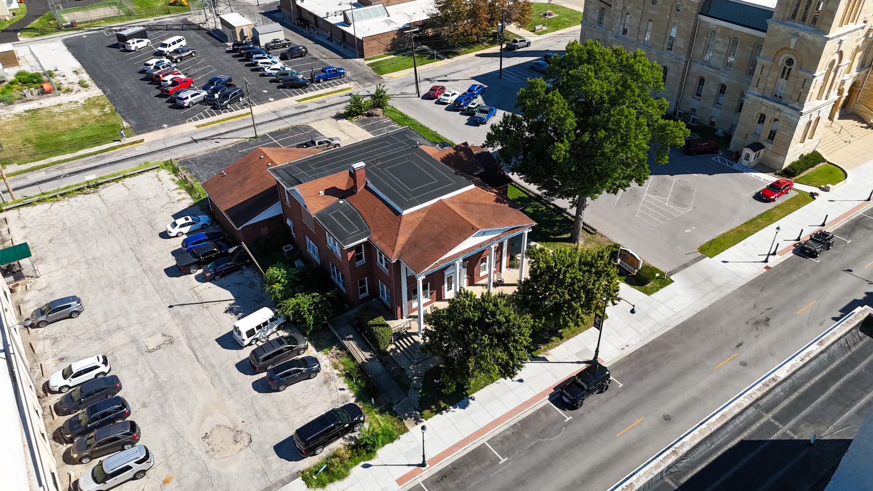 High aerial drone photo of the Gillham House and its parking lot on West State Street with the stone Morgan County Courthouse tower across the street in Jacksonville, Illinois
