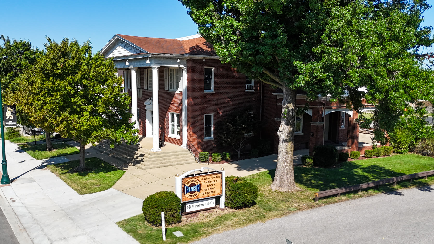 Drone photo of the two-story red brick Gillham House with tall white columns and the Jacksonville Transfer Company sign on the lawn, home of the antique mall in Jacksonville, Illinois