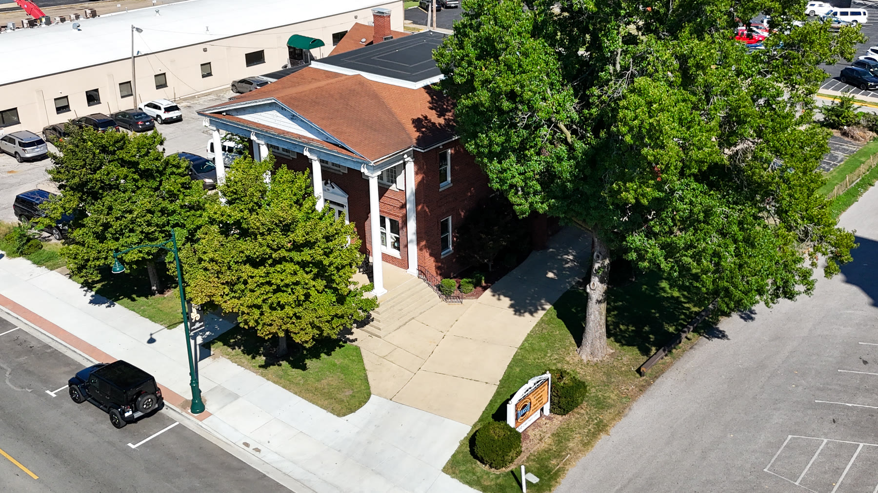 Aerial drone photo of the Gillham House on its corner lot along West State Street in Jacksonville, Illinois, with the sidewalk, street lamps, and shade trees