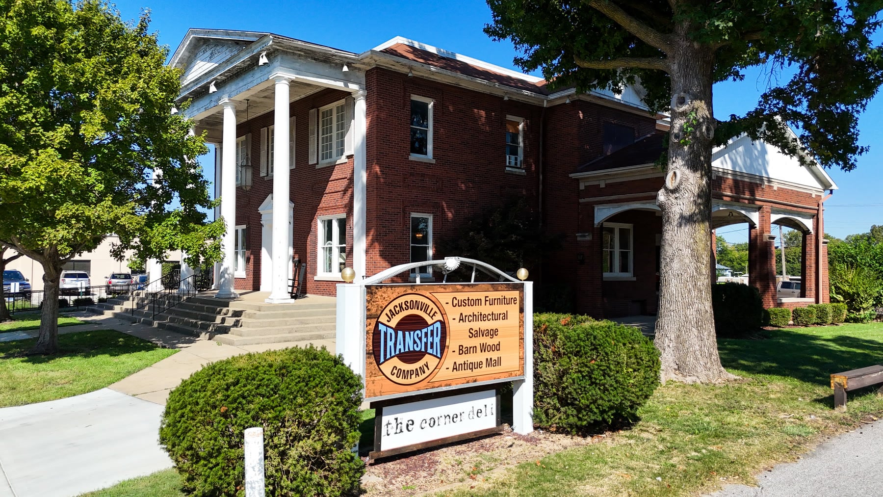 Low aerial drone photo of the Jacksonville Transfer Company sign listing custom furniture, architectural salvage, barn wood, and antique mall, in front of the red brick Gillham House with white columns at 326 W State St in Jacksonville, Illinois