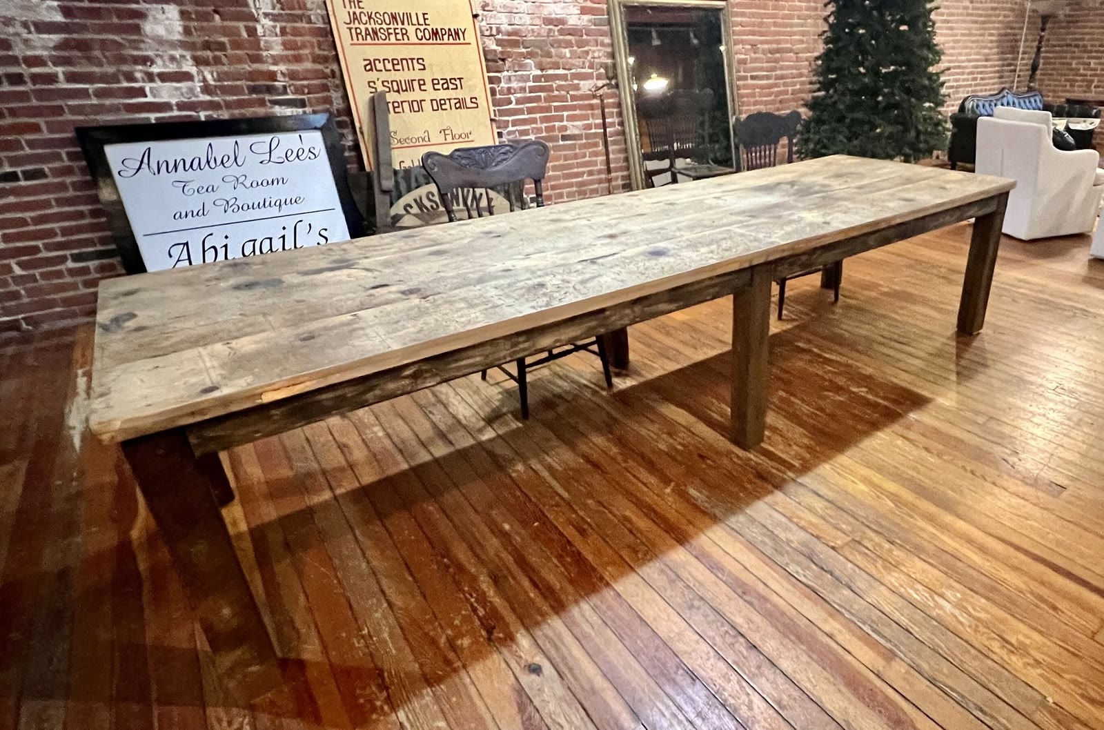 Long reclaimed wood farmhouse table with a trestle base on the wood floor of the Jacksonville Transfer Company showroom in Jacksonville, Illinois