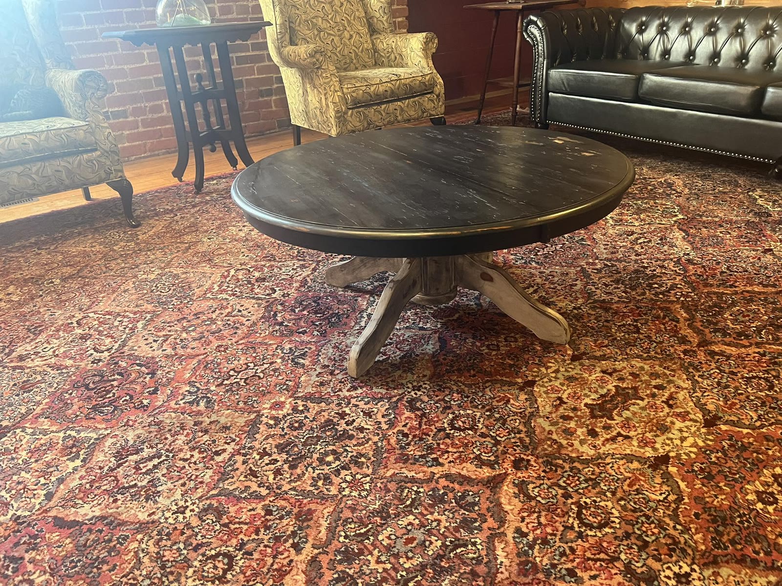 Round wooden pedestal table on a patterned antique rug with consigned armchairs and a leather sofa at Jacksonville Transfer Company in Jacksonville, Illinois